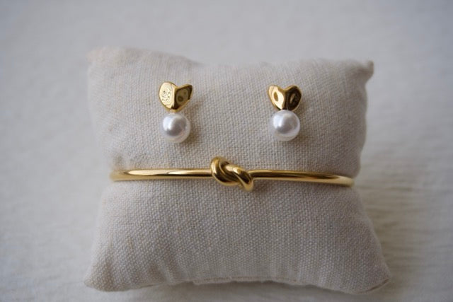 Gold bracelet and pearl earrings on a textured white surface